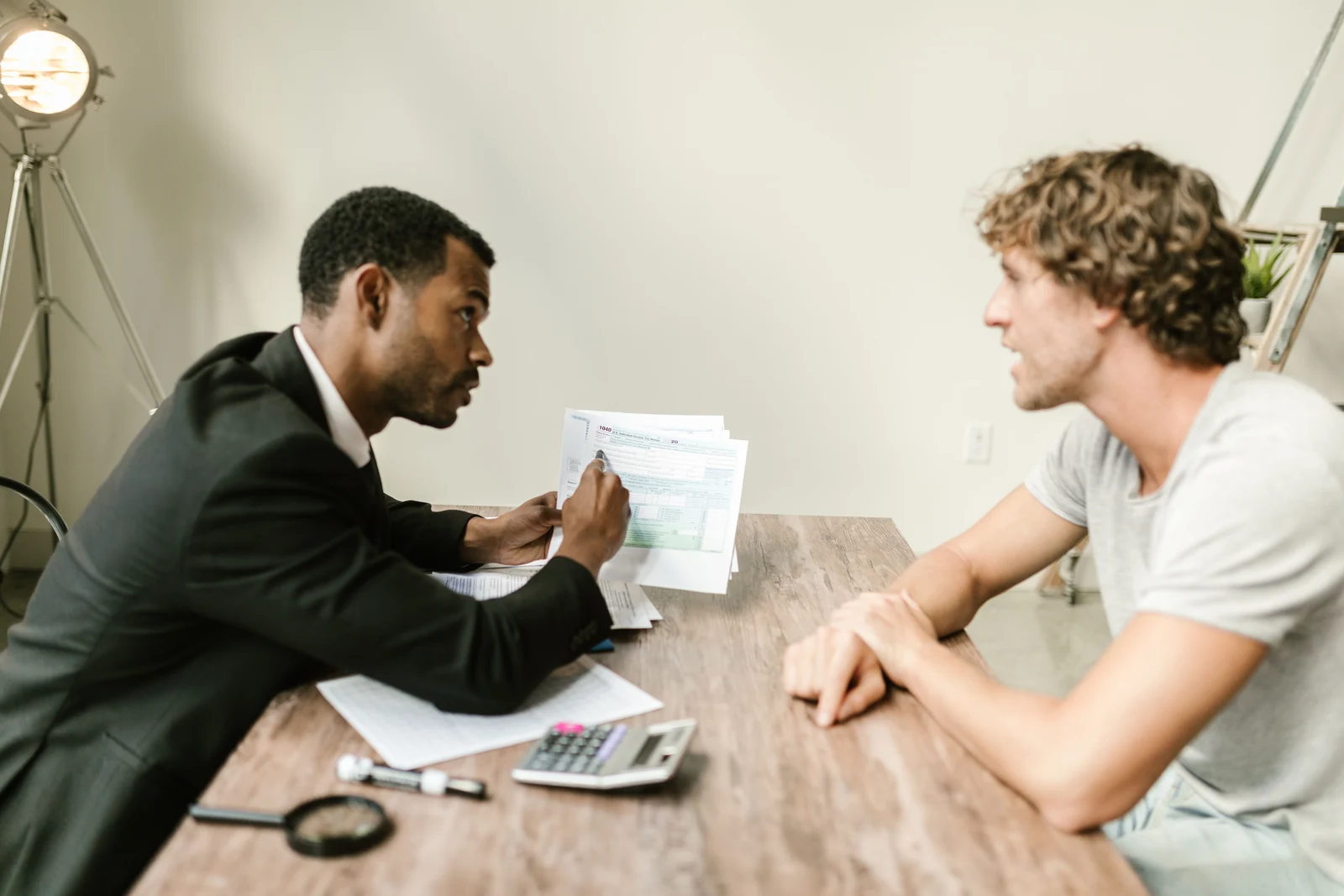 Two people discussing financial documents across a desk with a calculator.